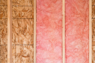 A person installing rolls of yellow BATT insulation in a new home